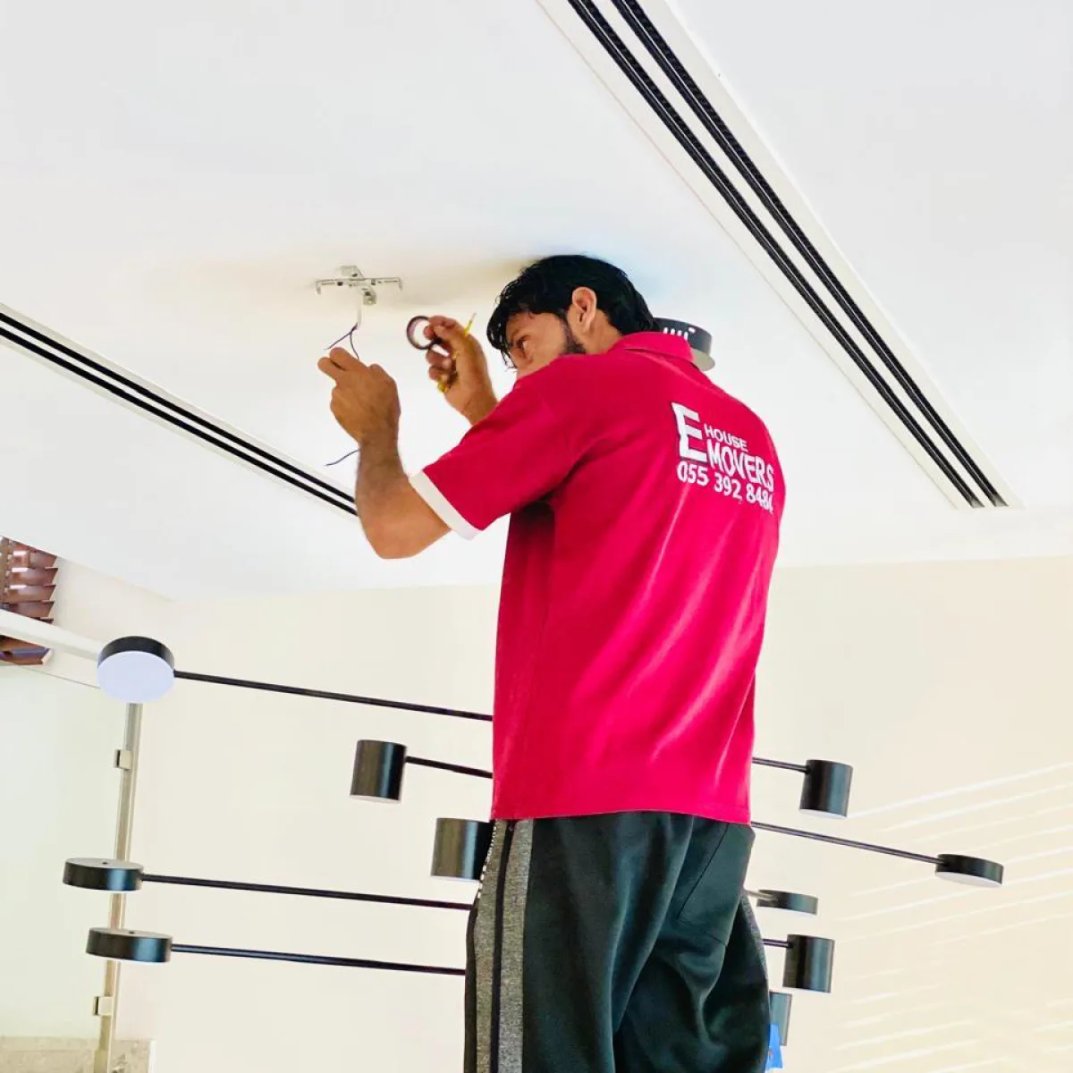 E House Movers mover fitting a ceiling light in an apartment