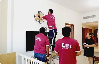 E House Movers team in uniform mounting a television during home relocation in Dubai