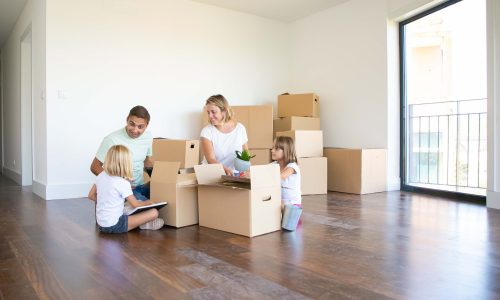 happy-parents-two-kids-moving-into-new-empty-apartment-sitting-floor-near-open-boxes